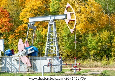 Oil rig pump rocking chair against the background of the autumn forest and sunset. Fuel, natural resources concept stock photo. Extraction of oil from a well using a pump