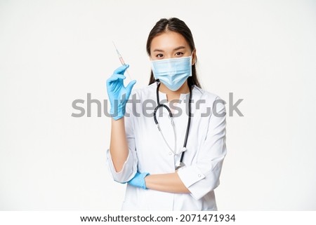 Vaccination and healthcare concept. Asian female doctor, nurse in medical face mask and gloves holding syringe with vaccine, white background Royalty-Free Stock Photo #2071471934