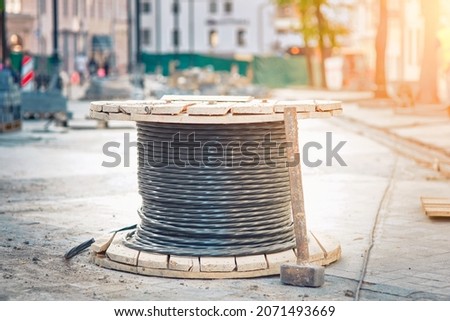 Spool with cable, wire spool - electric city communications, electricity supplying. Wooden coil with electric cable and optical fibers standing on the street, city street reconstruction.