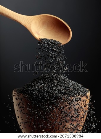 Grains of black sesame are poured with a wooden spoon in the bowl. Black sesame on a dark background. Copy space. Royalty-Free Stock Photo #2071508984