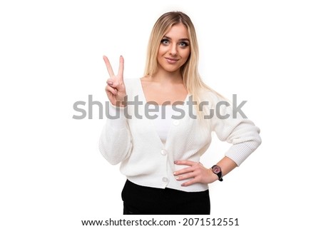Photo of a beautiful attractive pretty amazing charming young blonde woman with makeup in a stylish white knitted sweater and black pants shows two fingers isolated on a white background with empty
