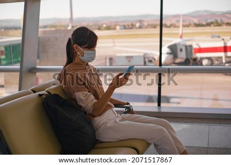 Woman traveler in face mask talk by phone as waiting for departure in airport. Female traveler wait in departure terminal Royalty-Free Stock Photo #2071517867