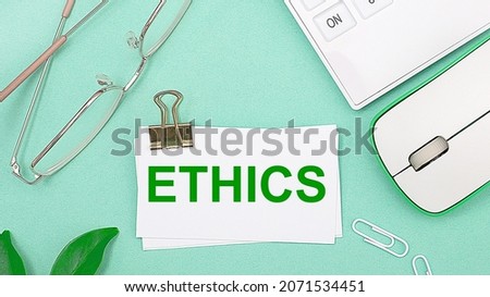 On a light green background there is a white calculator, a computer mouse, green leaves of a plant, gold-rimmed glasses and a white card with text ETHICS. Business concept
