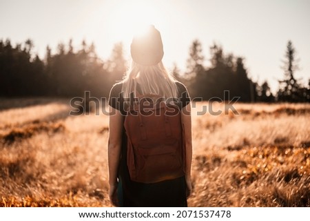  Young traveler hiking girl with backpacks. Hiking in nature. Sunset mood. Sunny landscape. Tourist traveler on background view mockup. Hiker looking sunlight in trip