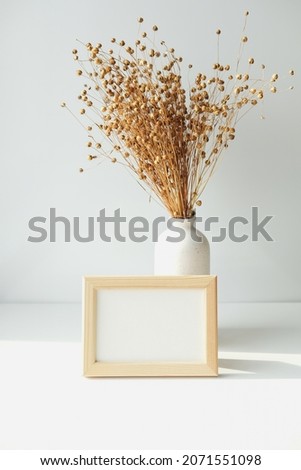 Photo frame mockup and vase with dried flax flowers on white background. Boho style living room interior decorations.