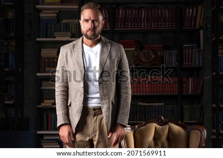 Handsome man posing in library near chair wearing suit in casual fashion style