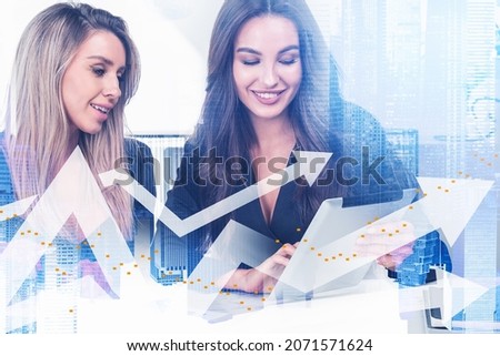 Two positive businesswomen in formal wears working together using tablet device. New York and Singapore skylines on background. Digital financial charts with arrows on foreground. Double exposure