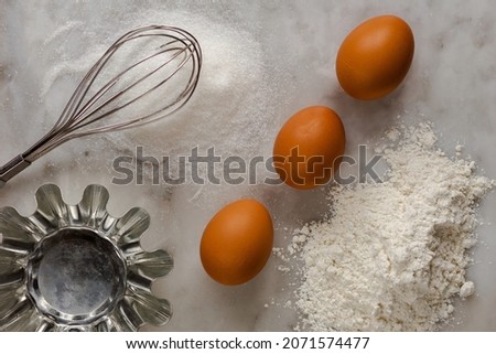 Top view of brown eggs, sugar, flour as ingredients, whisk and form for baking on marble background