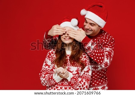 Young couple friends two man woman 20s in sweater hat close eyes with hands play guess who or hide and seek isolated on plain red background studio portrait. Happy New Year 2022 celebration concept
