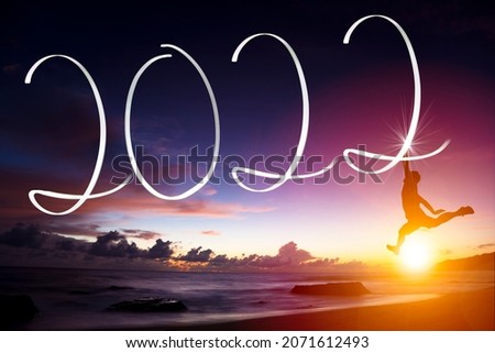 Man drawing 2022 by flashlight on the beach at sunrise.Happy new year 2022 concepts