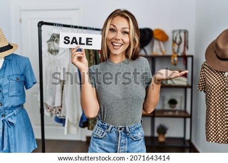 Young caucasian woman holding sale poster at retail shop celebrating achievement with happy smile and winner expression with raised hand 