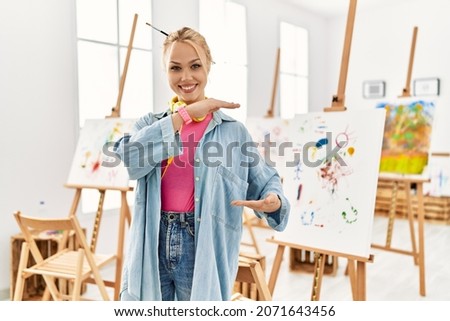 Young caucasian girl at art studio gesturing with hands showing big and large size sign, measure symbol. smiling looking at the camera. measuring concept. 