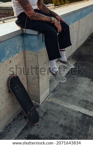 Close up of skaters legs. He is sitting on the wall and resting after ride while his skateboard leaning on the wall