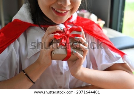 Cropped image of a beautiful woman holding a Christmas present box at the wooden table in the comfortable living room.
