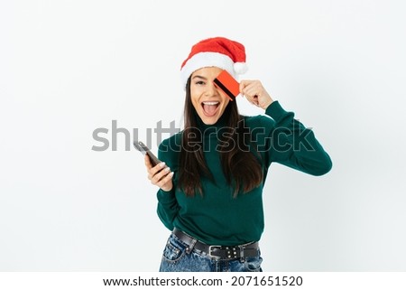 Young woman in santa hat with bank card and mobile phone on white background