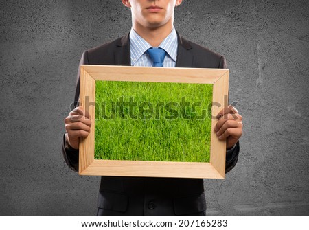 Close up of businessman holding frame with green grass