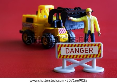 Toy forklift and a man - builder or road worker next to the danger sign. Hazard warning and prohibition signs concept. Red background. Close-up