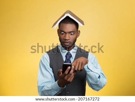 Closeup portrait surprised business man, executive reading, browsing news on smart phone holding mobile, book over head isolated yellow background. Human face expression, emotion, corporate lifestyle 