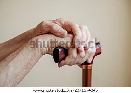 Macro shot of elderly woman's hands holding the wooden handle of a metal walking cane. Close up, copy space for text, neutral background. Royalty-Free Stock Photo #2071674845