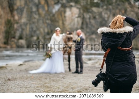 A photographer taking pictures of the bride and the groom with a horse