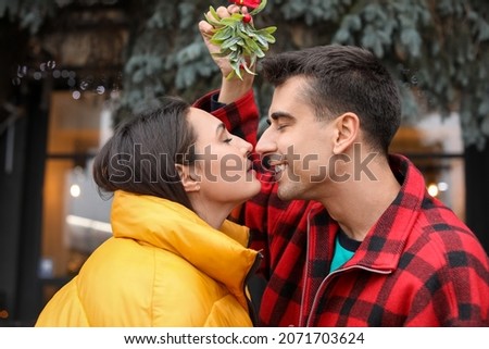 Young couple kissing under mistletoe branch outdoors on Christmas eve