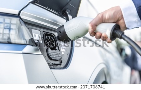 The driver of the electric car inserts the electrical connector to charge the batteries. Royalty-Free Stock Photo #2071706741