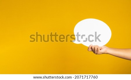 A speech bubble concept. Hand holding of an empty white speech balloon on yellow background with copy space for text. Close-up photo.