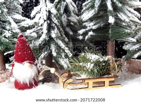 Christmas tree on wooden sled and gnome in the snow forest