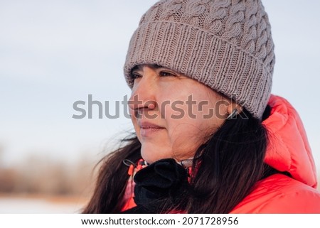Portrait of young woman. Beautiful brunette looks at winter forest and enjoys walk in nature after snowfall, winter frosty sunny morning. 