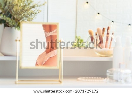 Reflection in table mirror of woman in underwear on dressing table with make up accessories. Self-Care. 