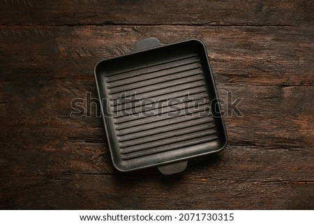 New empty cast-iron grill pan with two handles on wooden background. place for text. Flat lay top view black cast iron skillet for barbecue. Food Mockup Royalty-Free Stock Photo #2071730315
