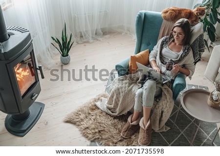 Remote work. Young woman using laptop in a cozy armchair and plaid sitting by the fireplace with a domestic cat and drinking tea at home Royalty-Free Stock Photo #2071735598