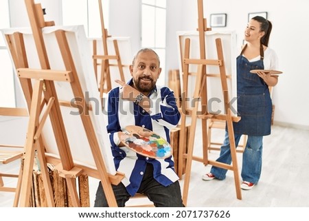 Senior artist man at art studio cheerful with a smile on face pointing with hand and finger up to the side with happy and natural expression 