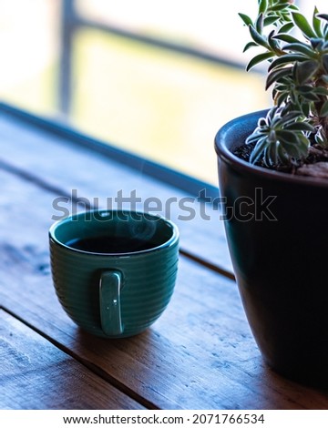Vertical view of a steaming cup of coffee on a wooden table and a succulent plant on the right.