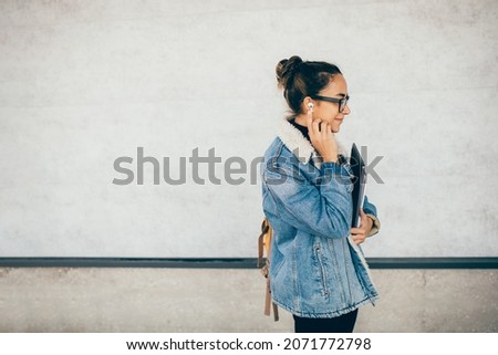Young happy student listening to music or podcast online using wireless earphones and smartphone. Modern technology.