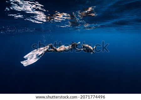 Lady with fins dive underwater with turtle in blue ocean.