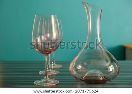 An empty wine carafe and three glasses in the interior sunny cuisine. Teal color background.