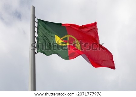 A large flag of Portugal is flying in a strong wind in a cloudy sky