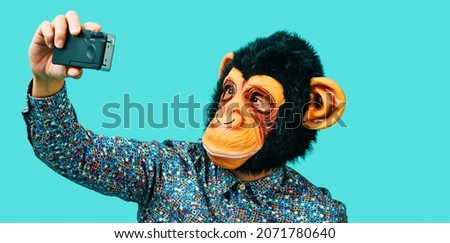 closeup of a man, wearing a monkey mask, taking a selfie with a retro film camera, on a blue background, in a panoramic format to use as web banner or header