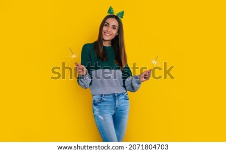 Close up photo of beautiful happy stylish woman in casual christmas sweater with sparklers in hands is posing isolated on yellow background and having fun
