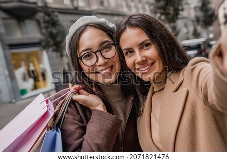 Two female friends women girlfriends with shopping bags making selfie outside in the city while doing shopping on black friday together.
