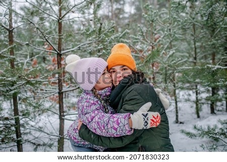 Pretty little girl kissing her mom with happiness that the first long-awaited snow has fallen, family walking in forest on snowing day, outdoor lifestyle, winter wonderland