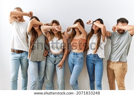 Group of young friends standing together over isolated background smiling cheerful playing peek a boo with hands showing face. surprised and exited 