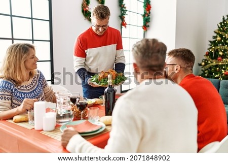 Group of middle age people meeting sitting on the table. Man standing and holding roasted turkey celebrating Christmas at home.