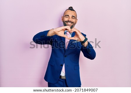 Young hispanic man wearing business suit and tie smiling in love doing heart symbol shape with hands. romantic concept. 