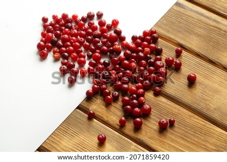 Many red cranberries on a white background and on a wooden background from pine boards. Rustic and modern styles. Diagonal. Close-up
