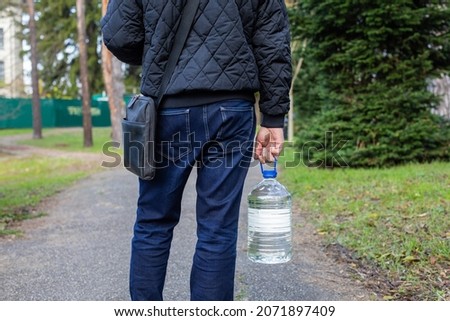 A man in jeans carries a bottle of water. 