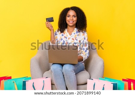 Photo of nice young wavy hairdo lady hold laptop shopping online sit on armchair wear shirt jeans isolated on yellow background