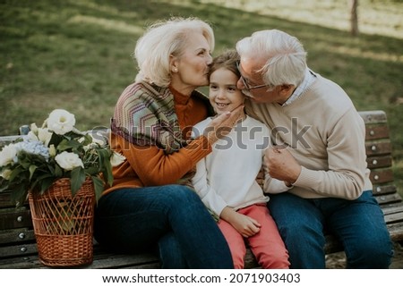 Heathy senior couple sitting on the bench witht heir cute little granddaughter Royalty-Free Stock Photo #2071903403