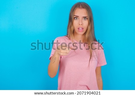 Shocked Beautiful caucasian girl wearing pink T-shirt over isolated background points at you with stunned expression